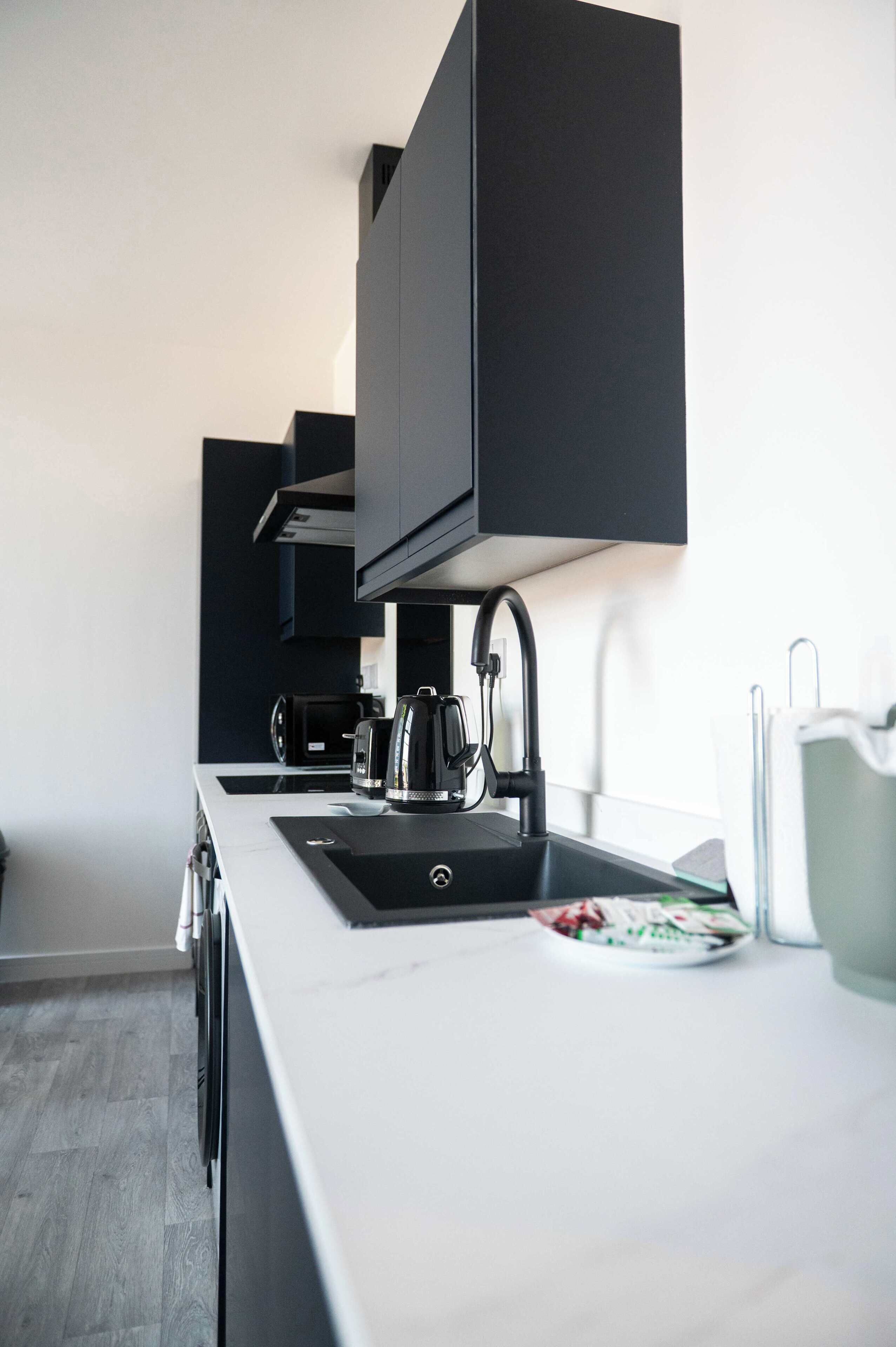 Una cocina moderna con encimera blanca, armarios negros, un hervidor y una cafetera.