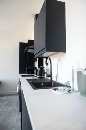 A modern kitchen with a white countertop, black cabinets, a kettle, and a coffee maker. - Modern 1 Bedroom Apartment in Derby with Parking (Derby)