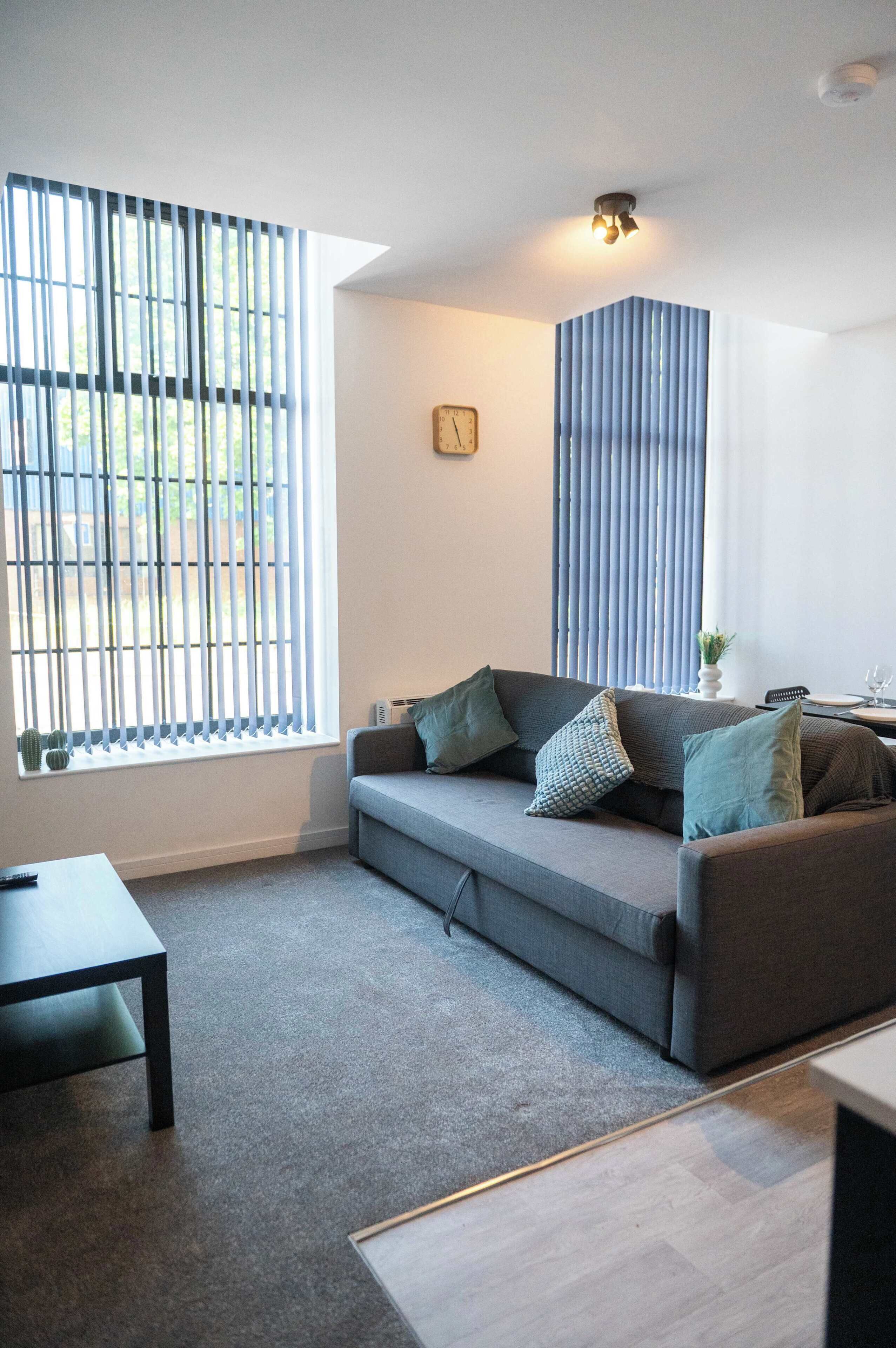 Un salón moderno con un sofá gris, una mesita y una ventana con persianas verticales.