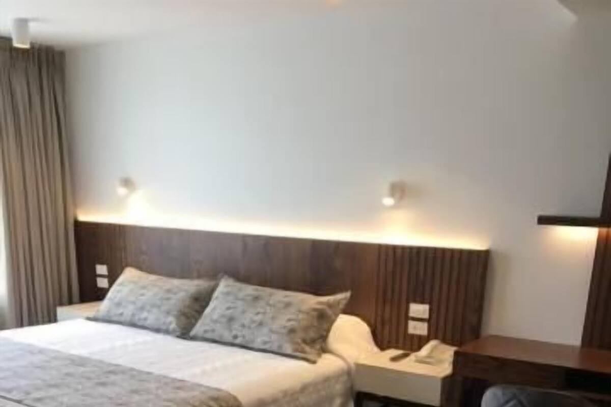 A hotel room with a bed, bedside table, chair, and a desk.