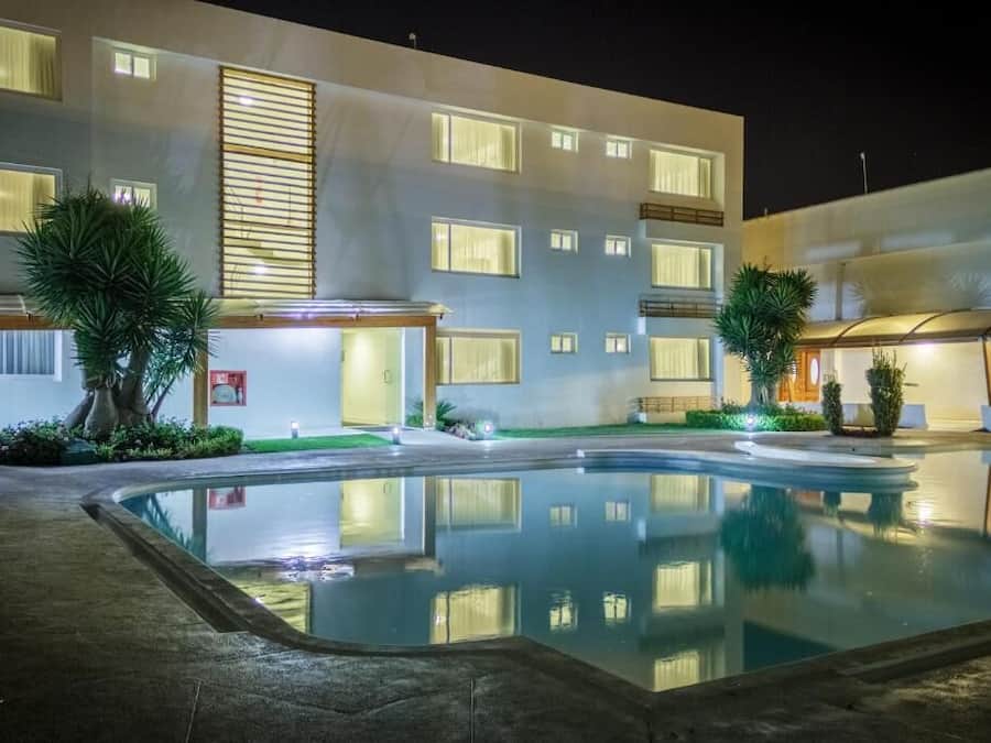 Un hotel moderno con piscina, varios balcones y ventanas bien iluminadas.