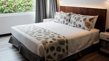 A neatly made bed with a patterned bedspread and pillows, a bedside table with a phone, and a window with curtains.