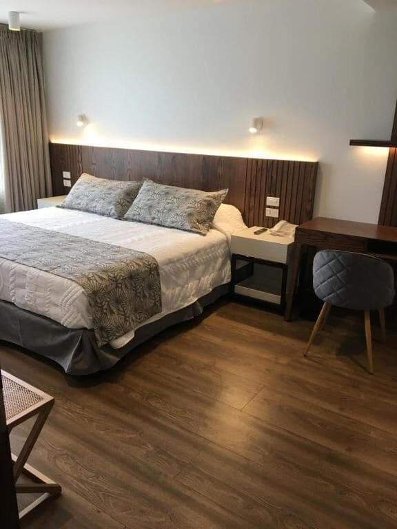 Een hotelkamer met een bed, nachtkastje, stoel en houten vloer.