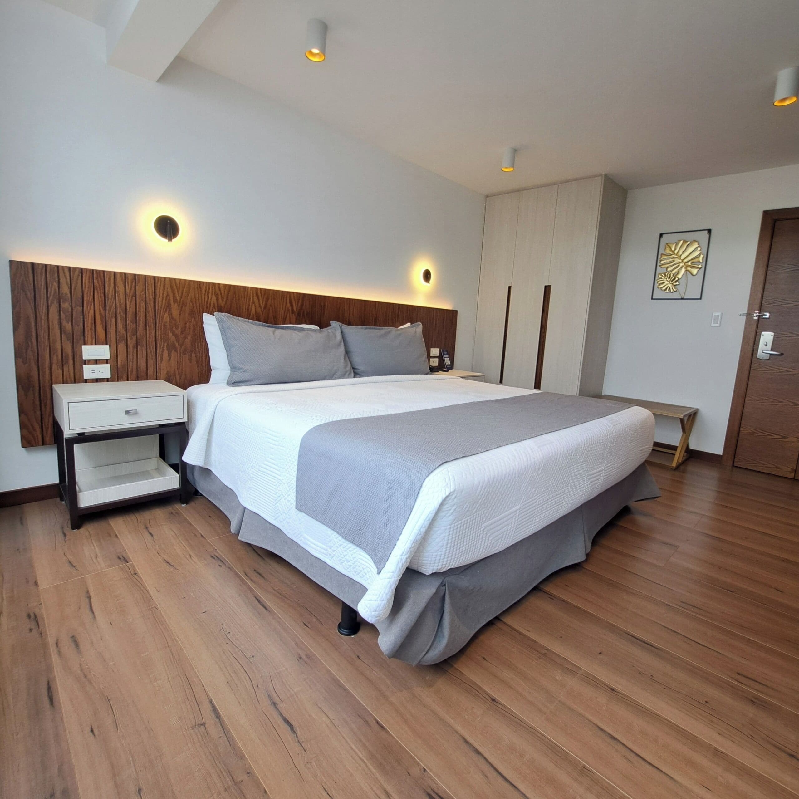 Een moderne slaapkamer met een houten hoofdbord, een bed met grijze beddengoed, een nachtkastje en een bijzettafeltje.
