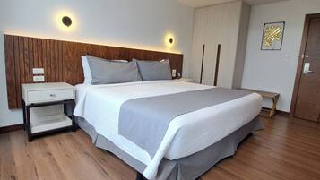 Een moderne slaapkamer met een houten hoofdbord, een bed met grijze beddengoed, een nachtkastje en een bijzettafeltje.