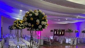 Une salle de banquet avec de longues tables dressées pour le repas, des chaises recouvertes de housses blanches et des centres de table floraux.