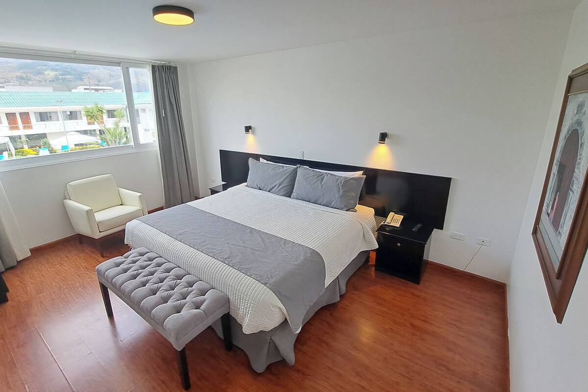 A modern hotel room with a large bed, bedside tables, a chair, and a view of buildings outside.