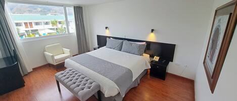 Una habitación de hotel moderna con una cama grande, mesitas de noche, una silla y vistas a edificios.