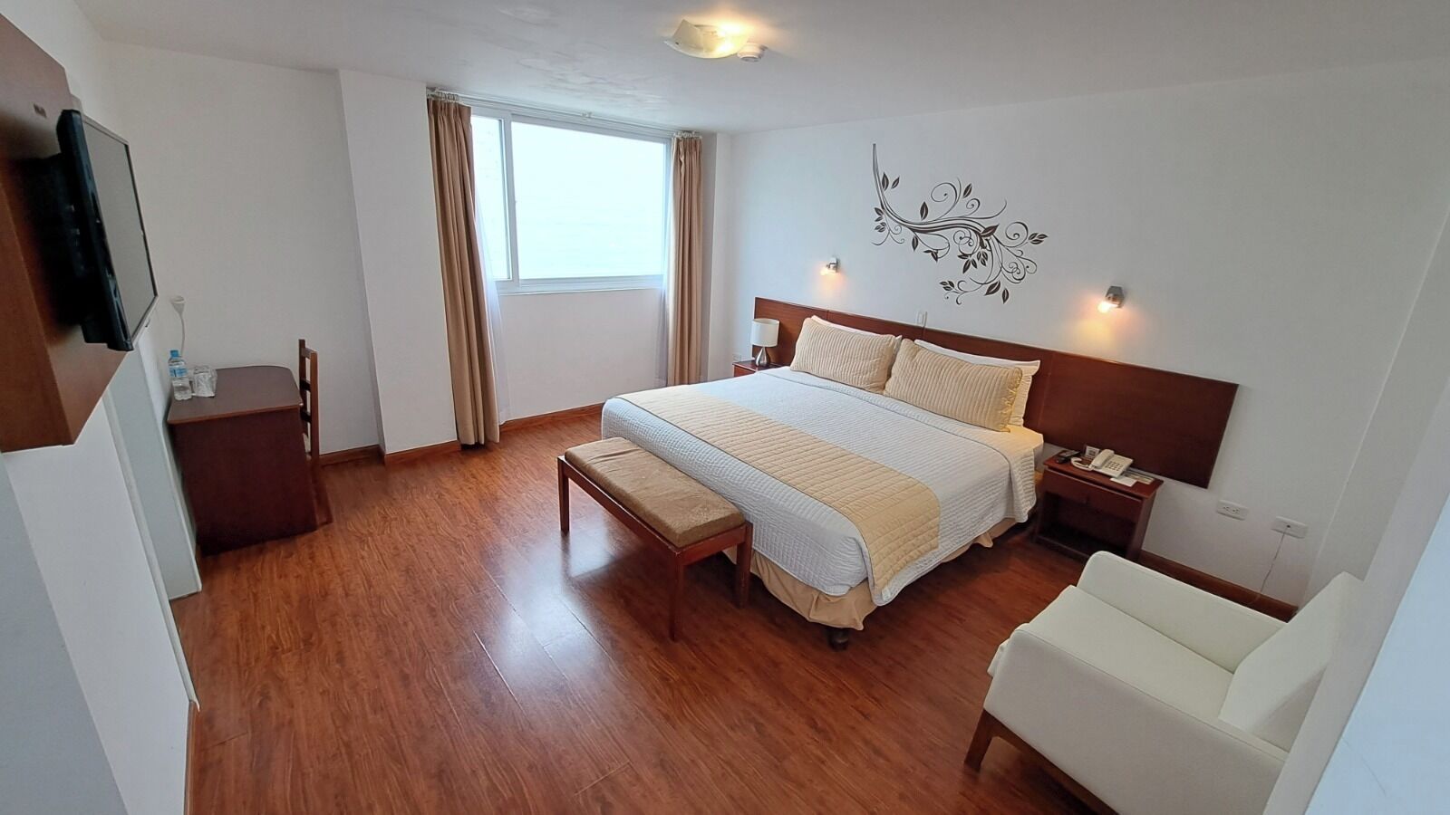 Habitación de hotel con cama, mesita de noche, silla y televisor montado en la pared.