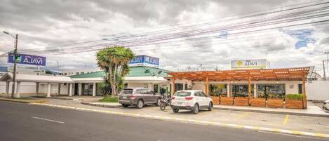 Zona comercial con edificios de AJAVI, un espacio de estar techado al aire libre y coches estacionados.