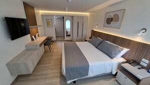Une chambre d’hôtel moderne, dotée d’un grand lit, d’une table de chevet, d’une télévision, d’un bureau et d’une chaise.