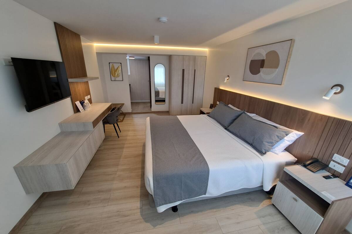 A modern hotel room with a large bed, bedside table, TV, desk, and chair.