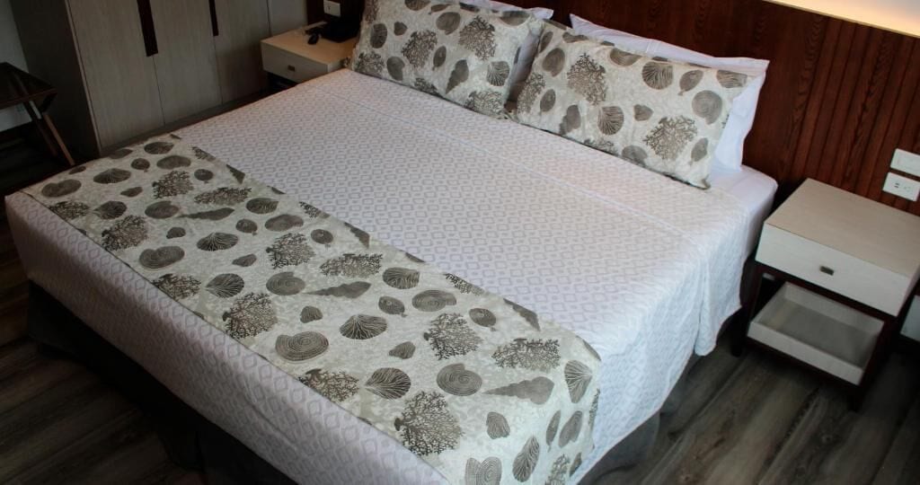 Una cama bien hecha con ropa de cama estampada, un cabecero de madera y una mesita de noche con un cajón.