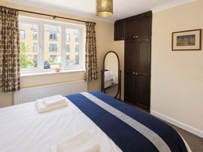 Ein Schlafzimmer mit Bett, einem Fenster mit Vorhängen, einem Heizkörper, einem Kleiderschrank und einem Spiegel.