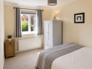 A bedroom with a bed, a radiator, a wardrobe, a bedside table with a plant, and a window with curtains.