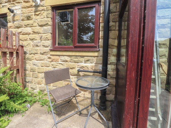A stone building with a window, a small round table, and a wicker chair. - Beckside Cottage (Hebden Bridge)