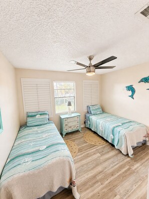 A bedroom with two beds, a ceiling fan, a window with blinds, and a wall decal. - Anastasia Hideaway 6 Min Walk to Beach Community Pool Near Dining & Amphitheatre (St. Augustine)
