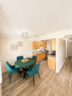 A dining area with a green table and teal chairs, a kitchen with wooden cabinets, and a sign that reads 'HAPPY PLACE'. - Anastasia Hideaway 6 Min Walk to Beach Community Pool Near Dining & Amphitheatre (St. Augustine)