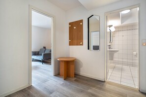 Un pasillo que conduce a un baño con lavamanos, espejo y una pequeña mesa de madera.