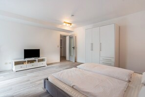 A bedroom with a bed, a TV on a stand, a wardrobe, and a door leading to another room. - Apartment 'Apt. Ringstr. 21, UG Links WE50' with Wi-Fi (Binz)