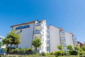 Ein mehrstöckiges Gebäude mit Balkonen, einem Schild mit der Aufschrift 'Grandruth' und einem strahlend blauen Himmel.