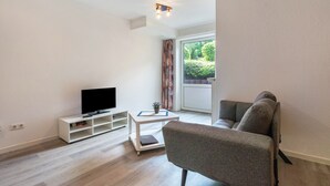 Una sala de estar moderna con una televisión de pantalla plana, un sofá, una mesa de centro y un ventanal corredero que da a un balcón.