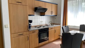 A compact kitchen with wooden cabinets, a gas stove, and a built-in oven. - Apartment 'Mais. Ringstr. 22, 3.OG Rechts WE48' with Balcony and Wi-Fi (Binz)