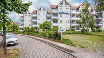 Un hôtel à plusieurs étages doté de balcons, d’une allée pavée et entouré de verdure.