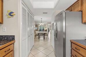 Eine Küche mit Edelstahl-Kühlschrank, Holzschränken, Fliesenboden und einem Essbereich mit Tisch und Stühlen.