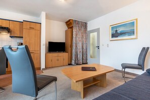 Un salon moderne avec une table en bois, deux chaises, un téléviseur et un tableau accroché au mur.