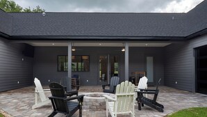 En overdækket terrasse med Adirondack-stole, bålsted og flisetapet gulv.