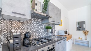 A modern kitchen with a gas stove, microwave, and a coffee maker. - Villa Latina Apartment in villa with garden, Wi-Fi and air conditioning (Solarino)