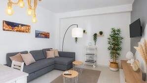 A modern living room with a grey sectional sofa, two round coffee tables, a white TV stand, and a large potted plant. - Villa Latina Apartment in villa with garden, Wi-Fi and air conditioning (Solarino)