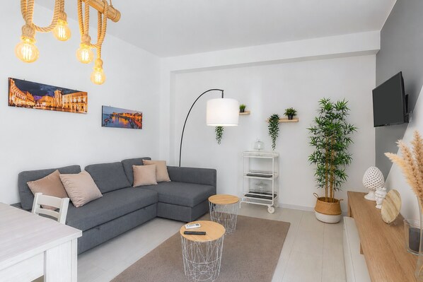 A modern living room with a grey sectional sofa, two round coffee tables, a white TV stand, and a large potted plant.