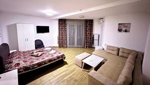 A hotel room with a bed, a sofa, a TV, a wardrobe, and a window with curtains. - Hotel Sunrise (Delchevo)