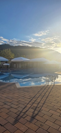 Une piscine avec une terrasse carrelée, un espace abrité doté de parasols et un paysage montagneux en arrière-plan.. Hotel Sunrise