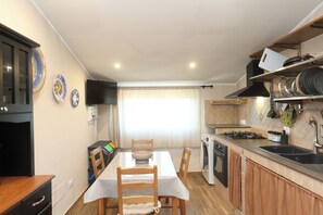 Una cocina con una mesa de comedor, sillas, un televisor, una ventana con cortinas y una estufa.