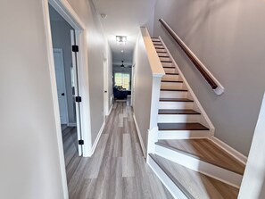 Ein Flur mit einer Holztreppe, einer Tür und einem Deckenventilator.