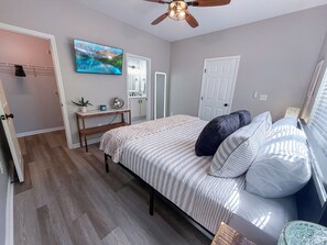 Ein Schlafzimmer mit einem Bett, einem Deckenventilator, einem Fernseher, einem Nachttisch und einer Tür.