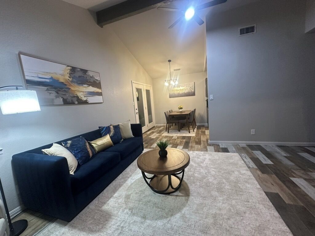 A living room with a sofa, a coffee table, a chandelier, and a dining area in the background.
