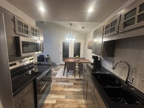 A modern kitchen with stainless steel appliances, a dining area with a table and chairs, and a black countertop sink. - Vine Cottage- A Spacious, charming home-Walk to the square and SWU! (Georgetown)