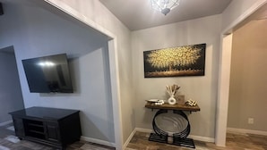 A hallway with a TV, a console table with decorative items, and a painting on the wall. - Vine Cottage- A Spacious, charming home-Walk to the square and SWU! (Georgetown)