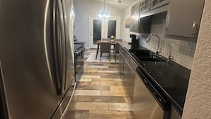 A modern kitchen with stainless steel appliances, a herringbone floor pattern, and a dining area with a chandelier. - Vine Cottage- A Spacious, charming home-Walk to the square and SWU! (Georgetown)
