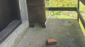 Un'area cucina esterna rustica con tavolo in legno, parete in mattoni e vista su un paesaggio verdeggiante.