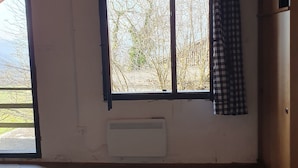 Una stanza con soffitto in legno, un'ampia finestra con vista sugli alberi, un termosifone e una tenda a quadri.