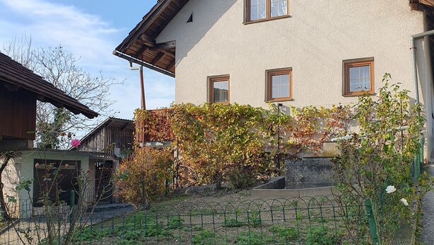 Una casa a due piani con tetto spiovente, un giardino con piante fiorite e un piccolo elemento d'acqua.