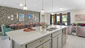 A modern kitchen with a marble island, pendant lights, and a dining area with a view. - NEW! Princess Theme! Minutes to Disney World! Private Pool and Hot tub! Theatre! (Kissimmee)
