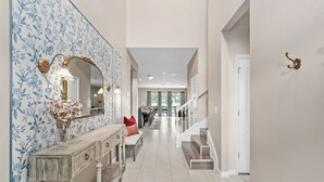 A hallway with a floral wallpaper, a console table with a mirror, a bench, and a staircase. - NEW! Princess Theme! Minutes to Disney World! Private Pool and Hot tub! Theatre! (Kissimmee)