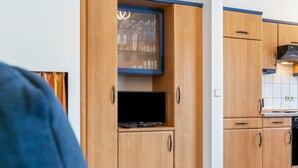 Cuina moderna amb armaris de fusta, televisió integrada i un armari amb portes de vidre a la part superior.