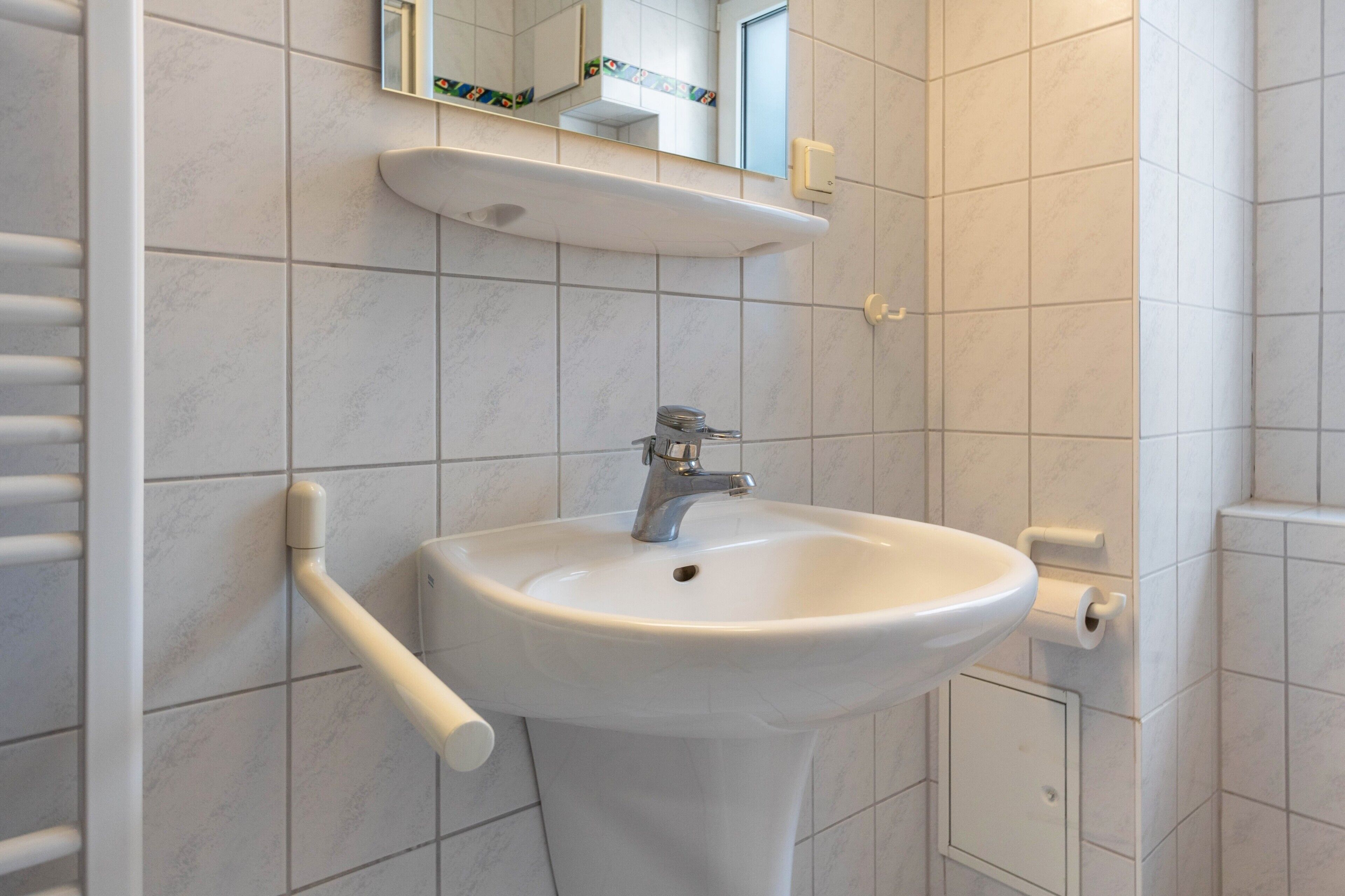 Ein Badezimmer mit weißem Waschbecken, einem Spiegel und einem Handtuchhalter.